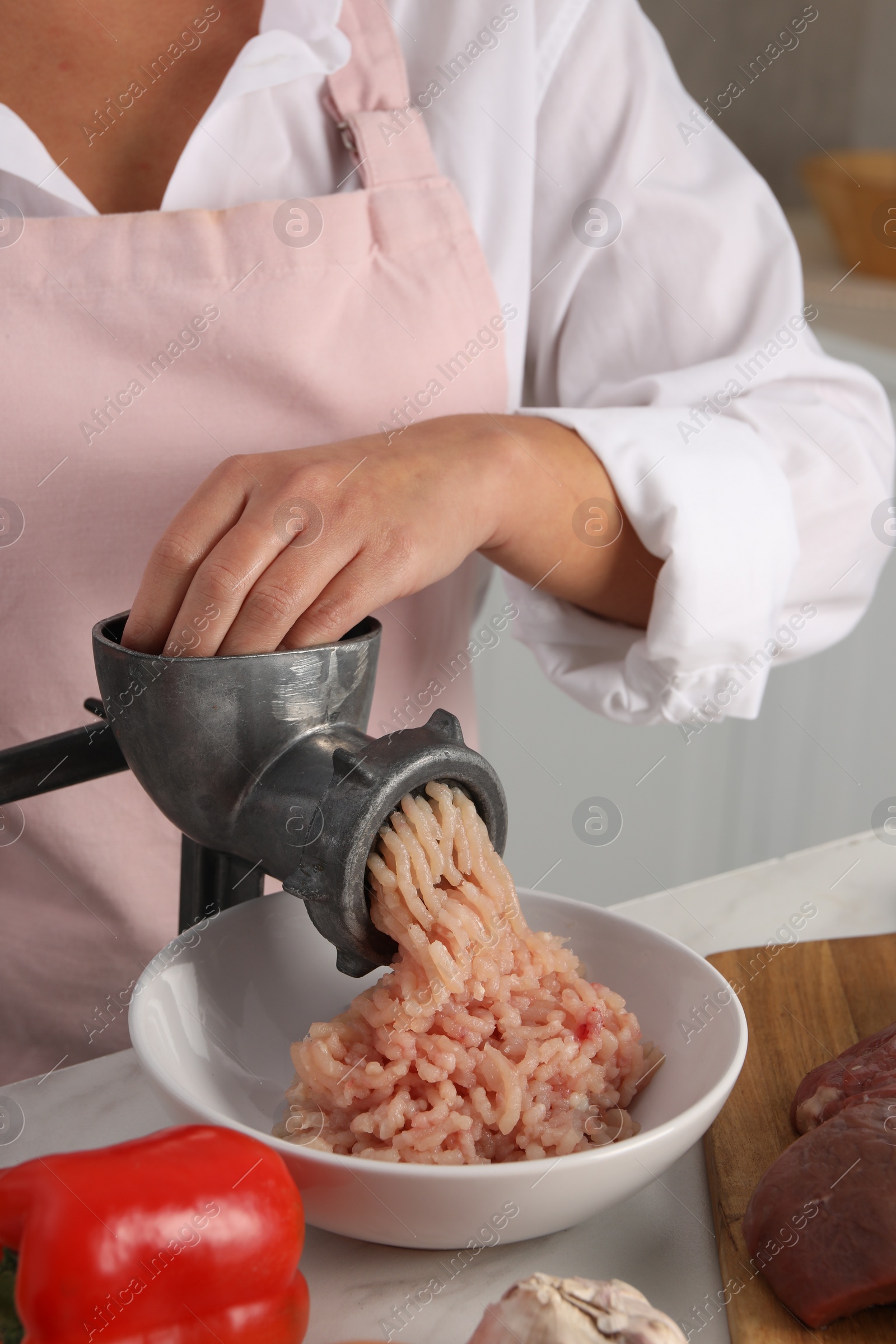 Photo of Woman making chicken mince with metal meat grinder at white table in kitchen, closeup