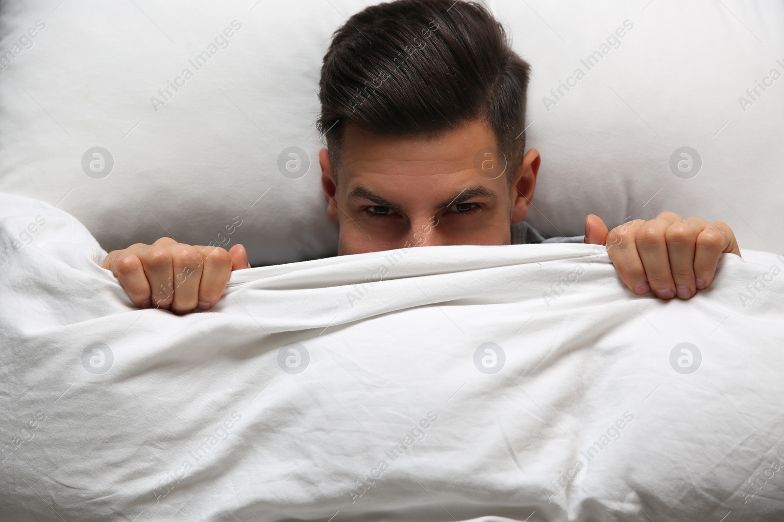 Photo of Handsome man covering his face with blanket while lying in bed at home