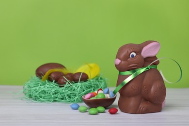 Chocolate Easter bunny, eggs and candies on white wooden table against light green background