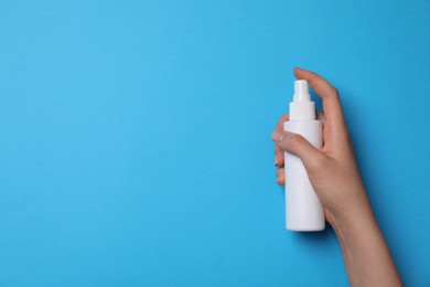 Woman holding hand sanitizer on light blue background, closeup view with space for text. Safety equipment