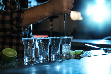 Photo of Bartender pouring Mexican Tequila into shot glasses at bar counter, closeup