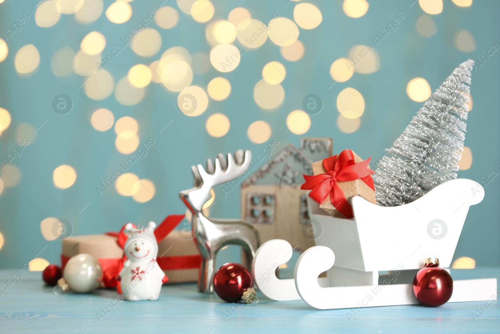 Photo of White sleigh with gift boxes and Christmas decor on light blue table against blurred lights