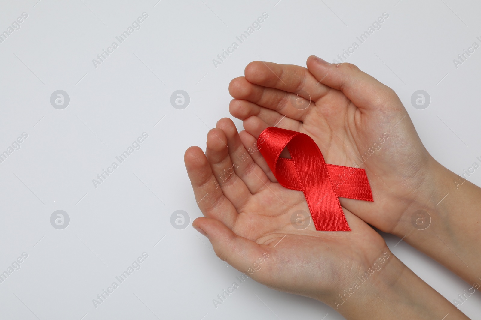 Photo of Little girl holding red ribbon on white background, closeup. AIDS disease awareness