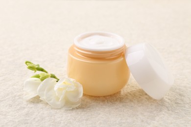 Body care. Moisturizing cream in open jar and flower on light textured table, closeup