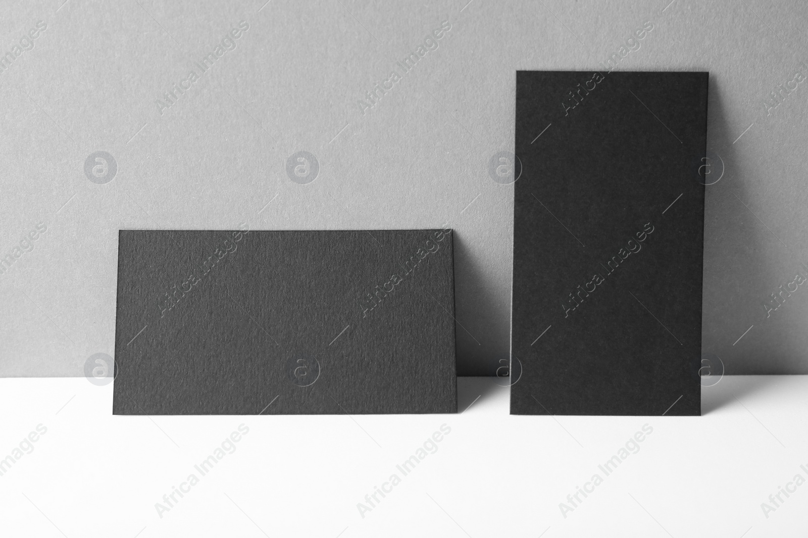 Photo of Blank black business cards on white table against grey background. Mockup for design