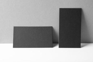 Photo of Blank black business cards on white table against grey background. Mockup for design