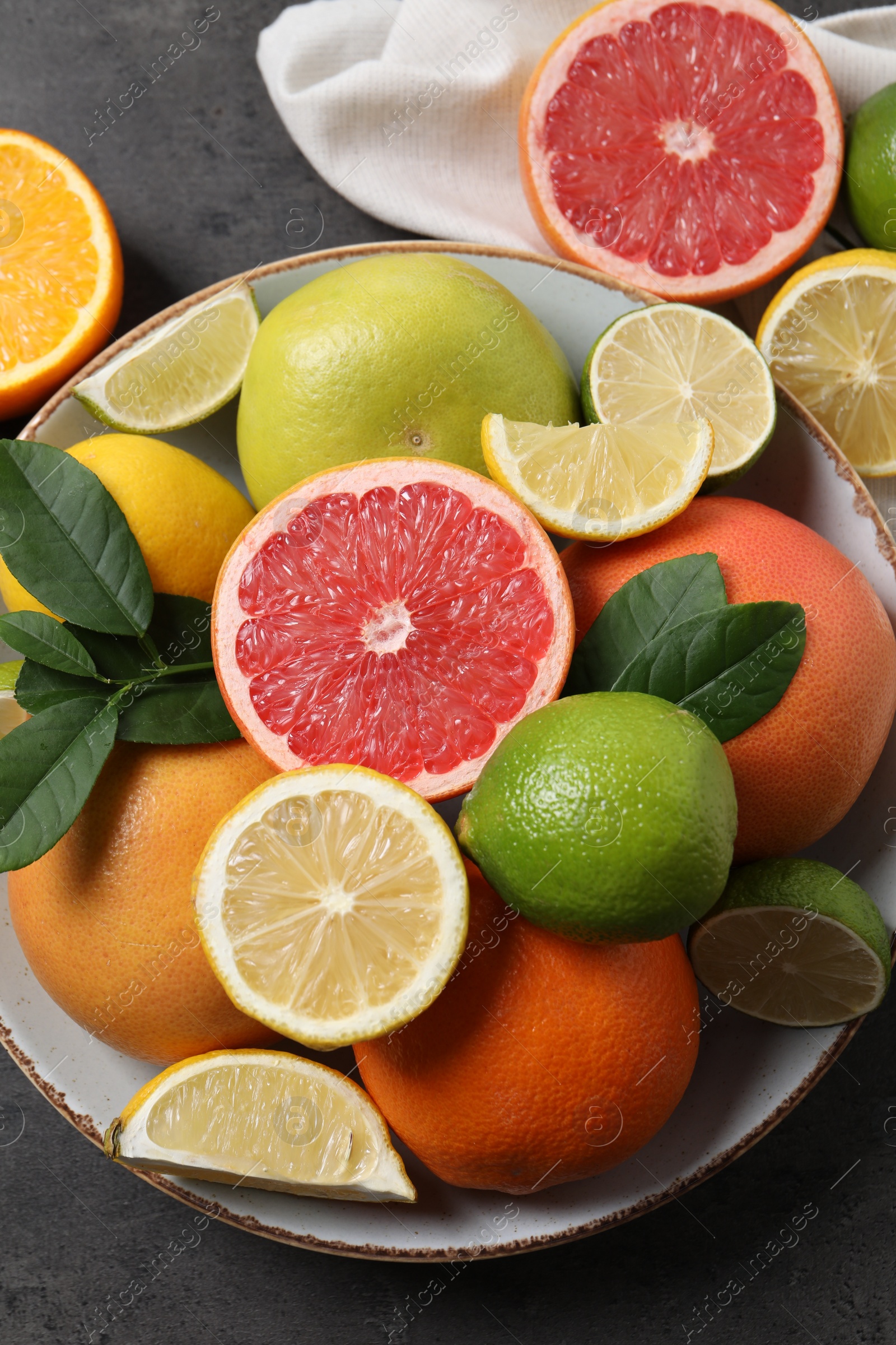 Photo of Different fresh citrus fruits and leaves on grey textured table, flat lay