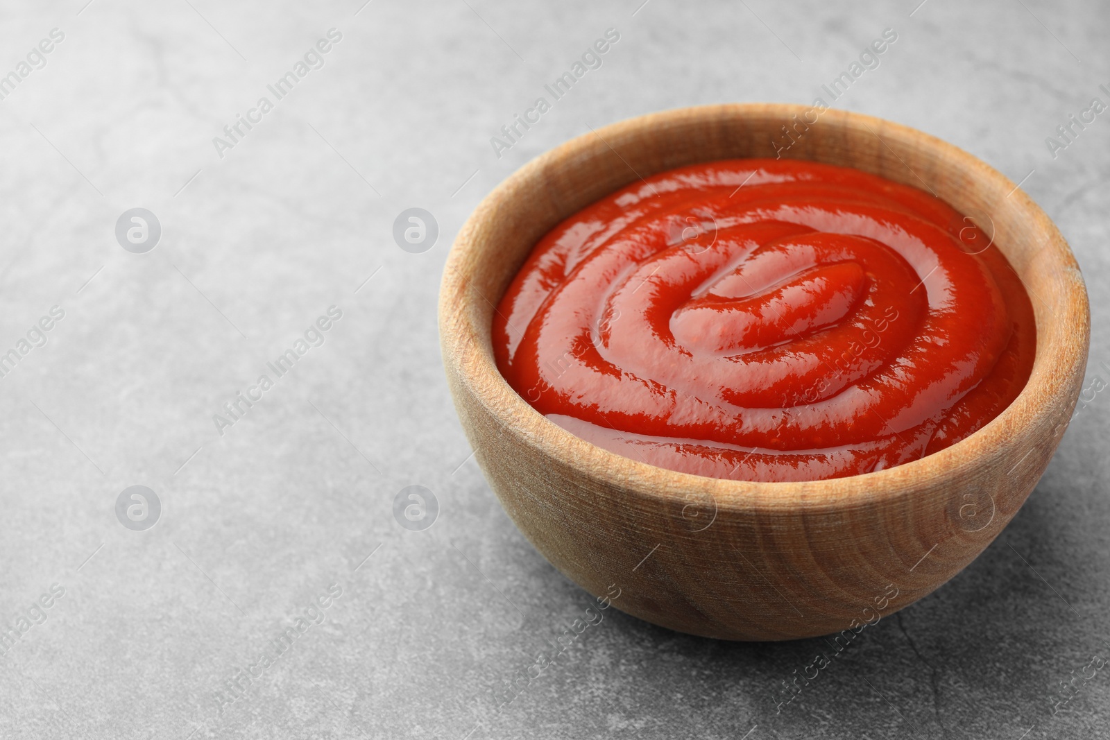 Photo of Bowl of tasty ketchup on light grey table, closeup. Space for text