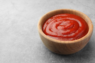 Bowl of tasty ketchup on light grey table, closeup. Space for text