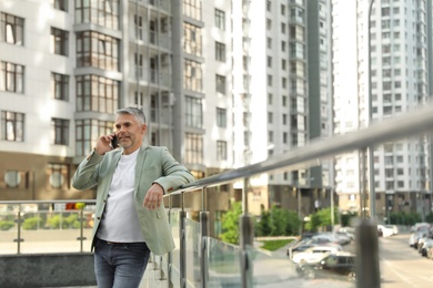 Photo of Handsome mature man talking on phone in city center. Space for text