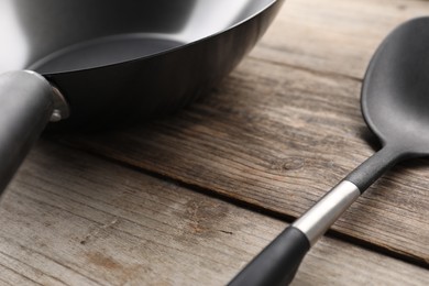 Photo of Black metal wok and spatula on wooden table, closeup