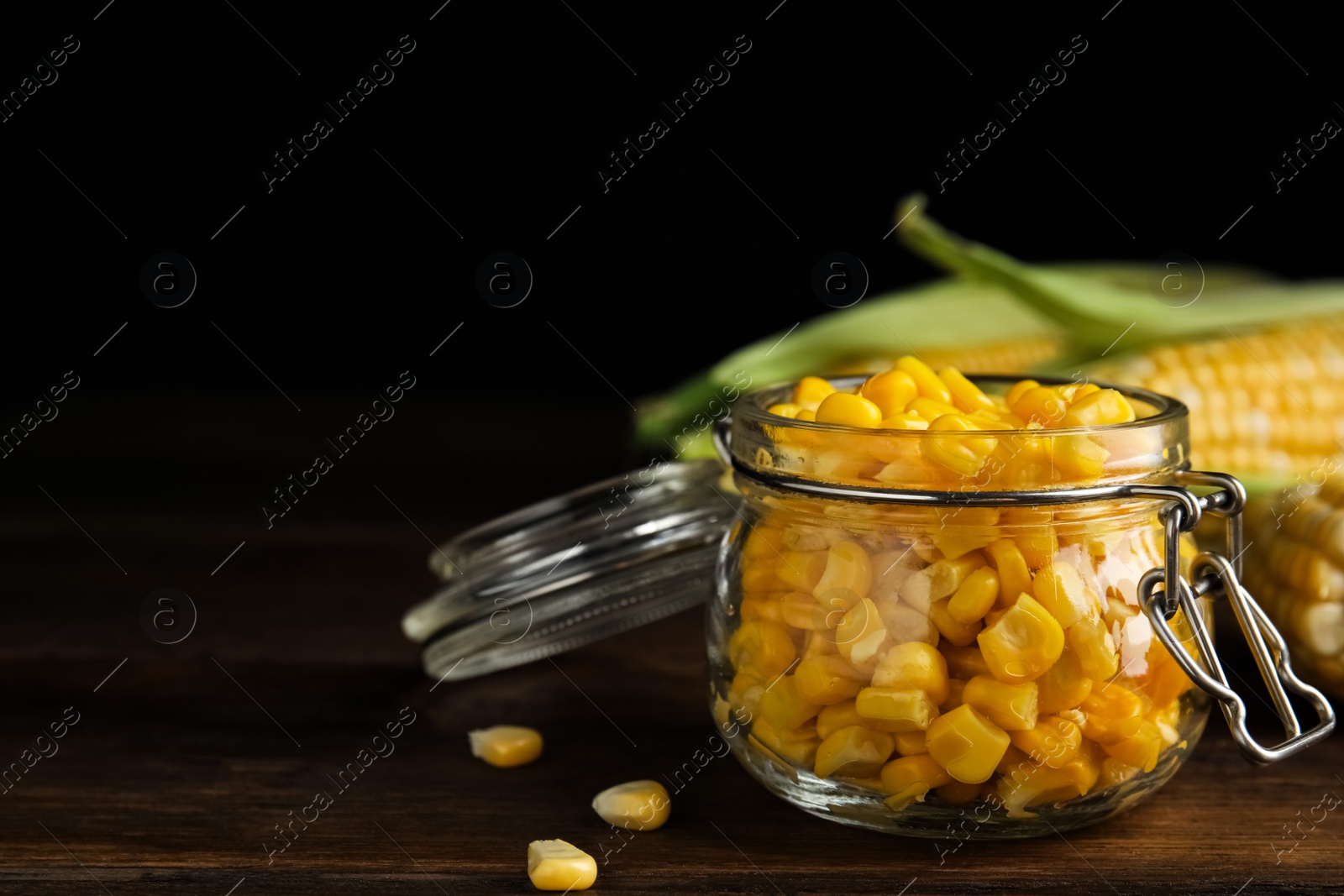 Photo of Tasty sweet corn kernels in jar on wooden table. Space for text