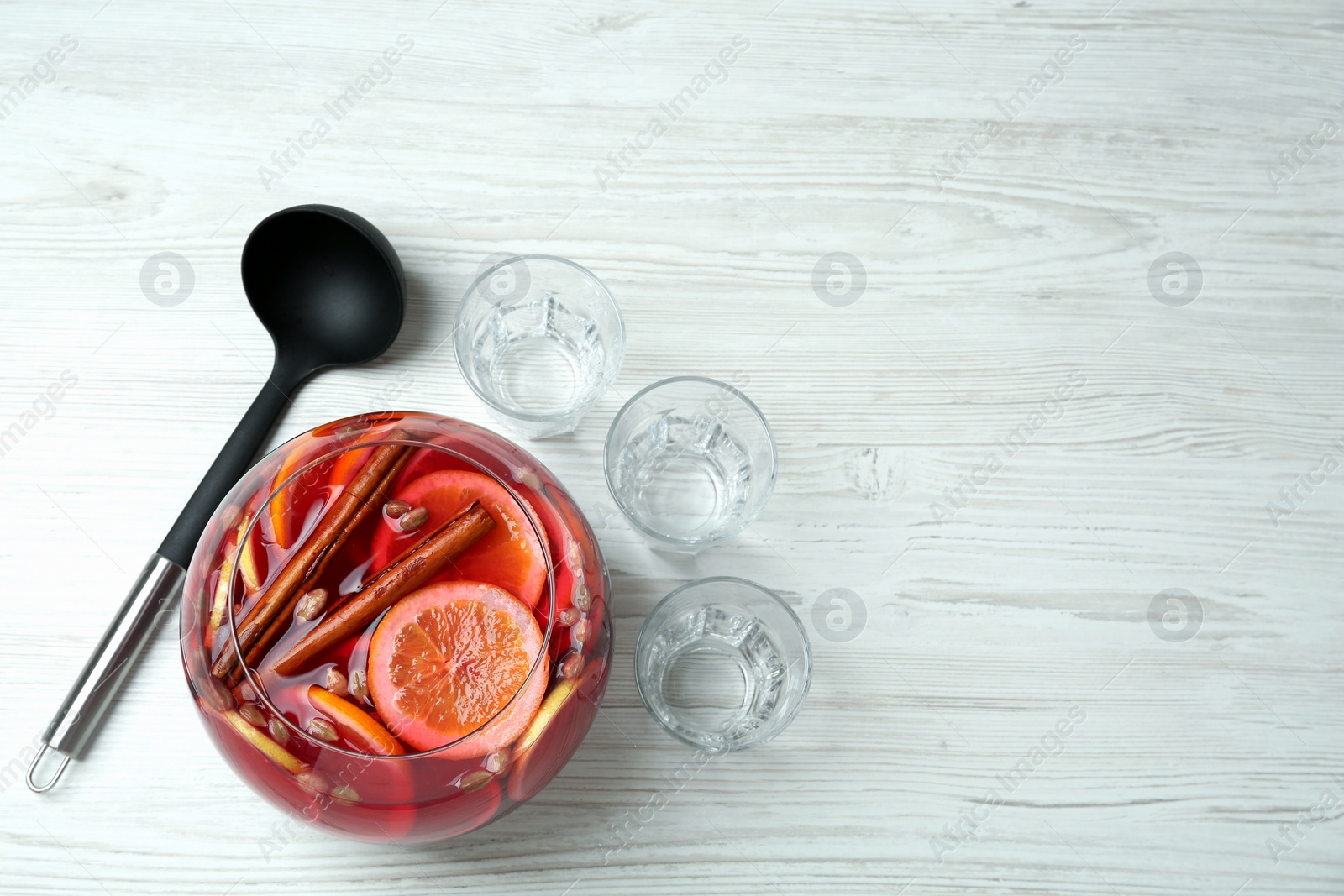 Photo of Empty glasses and ladle near bowl of aromatic punch drink on white wooden table, flat lay. Space for text