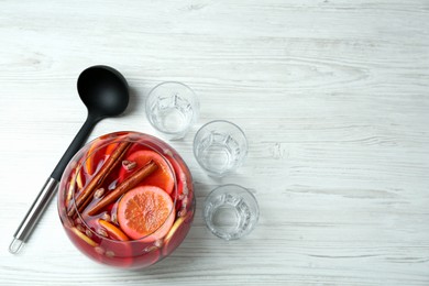 Photo of Empty glasses and ladle near bowl of aromatic punch drink on white wooden table, flat lay. Space for text