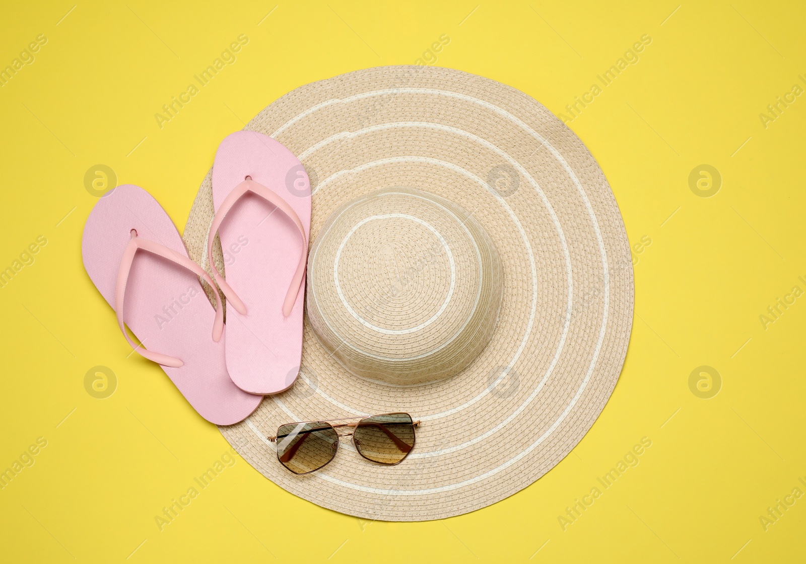 Photo of Flip flops, hat and sunglasses on yellow background, flat lay. Beach objects