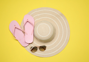 Flip flops, hat and sunglasses on yellow background, flat lay. Beach objects