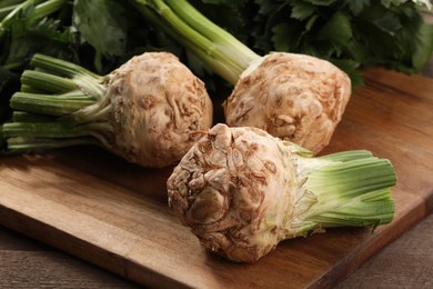 Photo of Fresh raw celery roots and leaves on wooden table, closeup