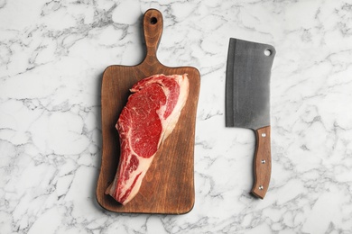 Board with fresh raw beef meat and butcher knife on white marble table, flat lay