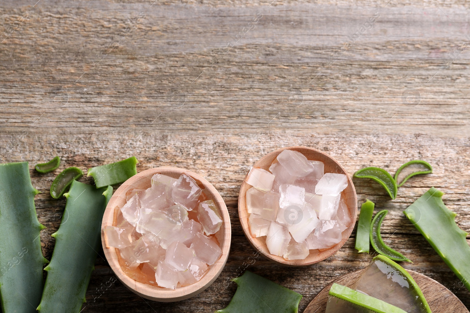 Photo of Aloe vera gel and slices of plant on wooden table, flat lay. Space for text