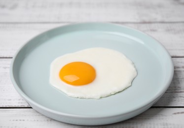 Tasty fried egg in plate on white wooden table, closeup