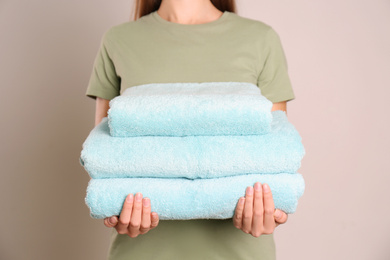 Woman holding stack of fresh towels on grey background, closeup