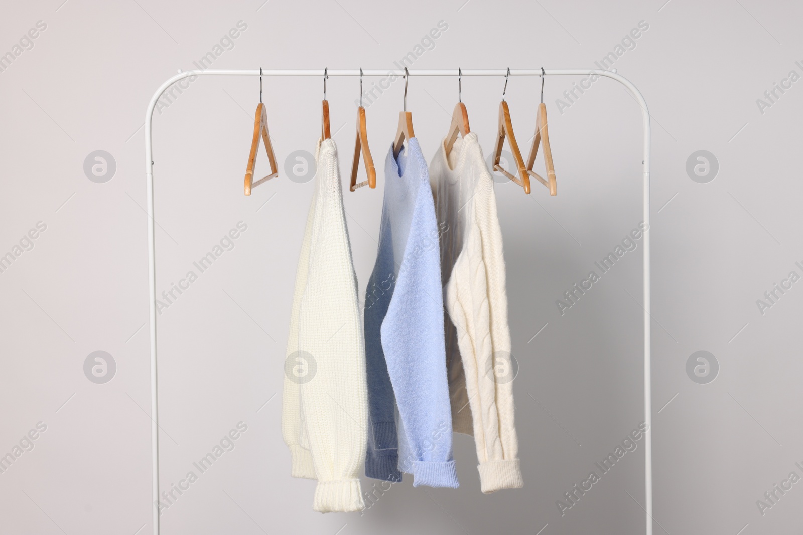 Photo of Rack with different warm sweaters on light background