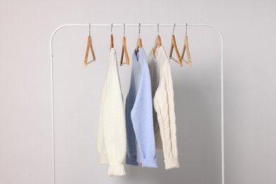 Rack with different warm sweaters on light background