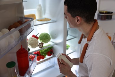 Man with sauce and sausages near refrigerator in kitchen