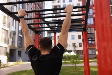 Man training on monkey bars at outdoor gym, back view
