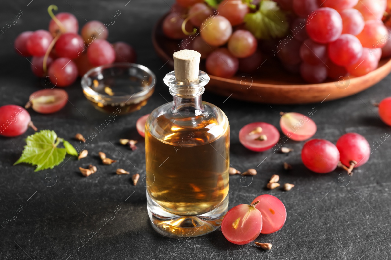 Photo of Organic red grapes, seeds and bottle of natural essential oil on black table