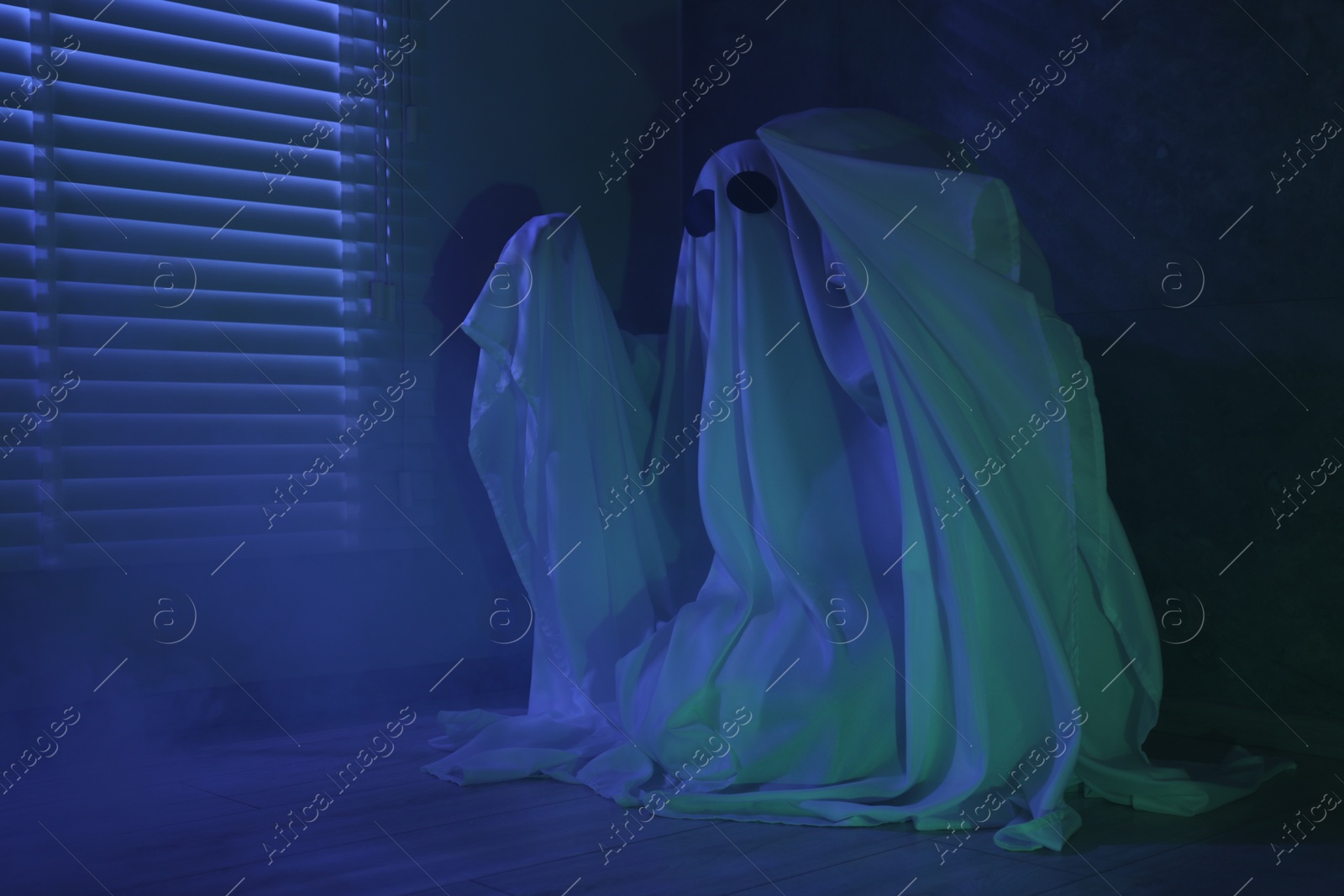 Photo of Creepy ghost. Woman covered with sheet near window in blue light