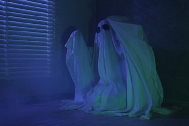 Creepy ghost. Woman covered with sheet near window in blue light