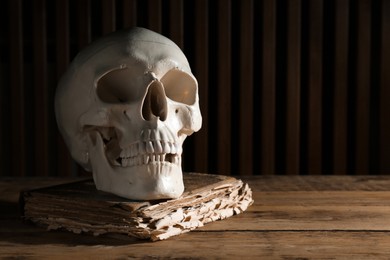 Photo of Human skull and old book on wooden table, space for text