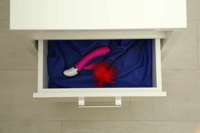 Photo of Vibrator and feather tickler in drawer indoors, top view. Sex toys