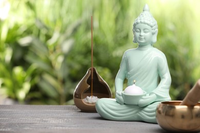 Photo of Buddhism religion. Decorative Buddha statue with burning candle, incense stick and singing bowl on wooden table outdoors, space for text