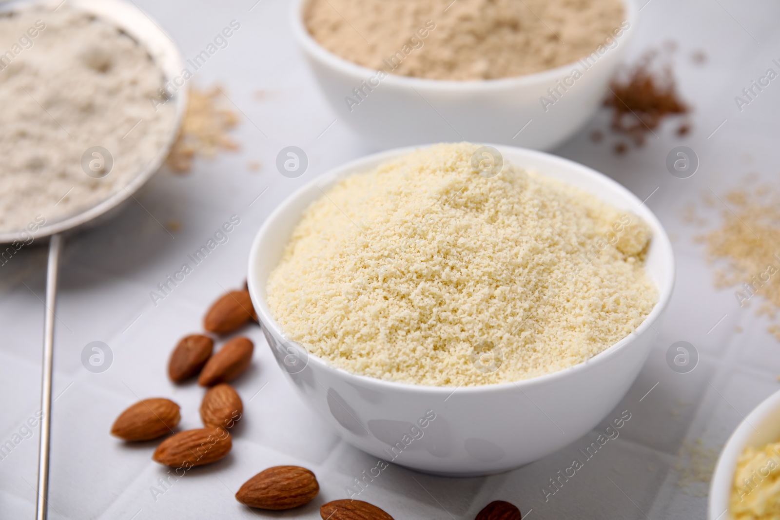 Photo of Bowls with different types of flour on tiled table, closeup