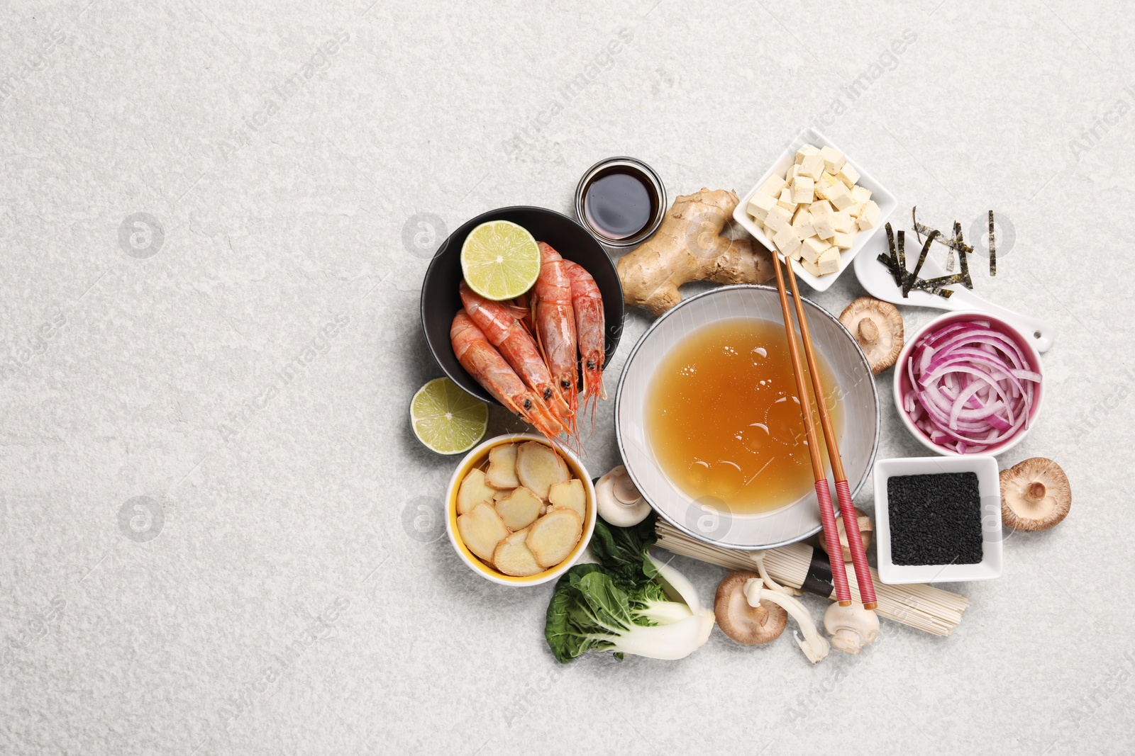 Photo of Cooking delicious ramen soup. Different ingredients and chopsticks on beige table, flat lay. Space for text
