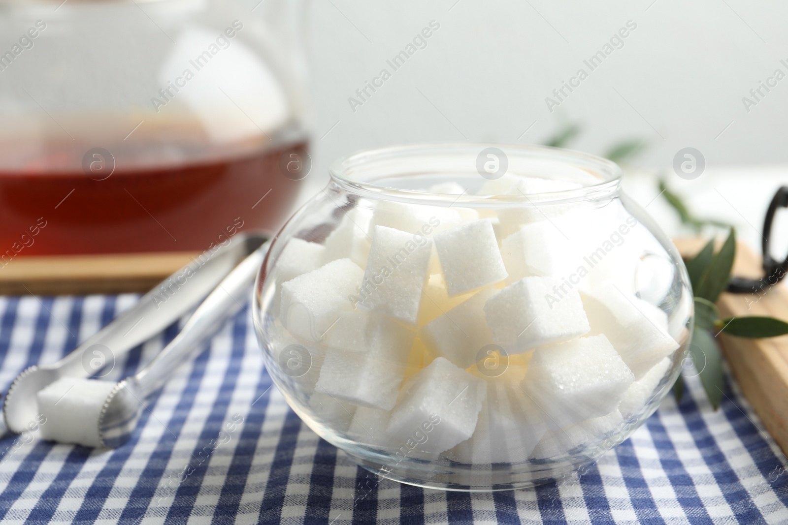 Photo of Refined sugar cubes in glass bowl and tongs on wooden tray, closeup