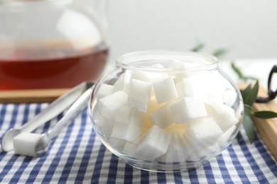 Photo of Refined sugar cubes in glass bowl and tongs on wooden tray, closeup