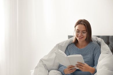 Photo of Young woman in warm sweater reading book on bed at home. Space for text