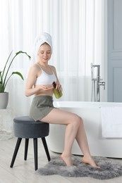 Photo of Beautiful young woman applying oil onto hand in bathroom