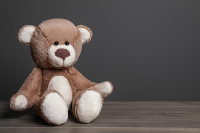 Photo of Cute teddy bear on wooden table near black wall, space for text