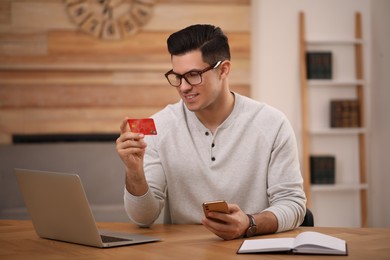 Photo of Man using smartphone and credit card for online payment at desk in room