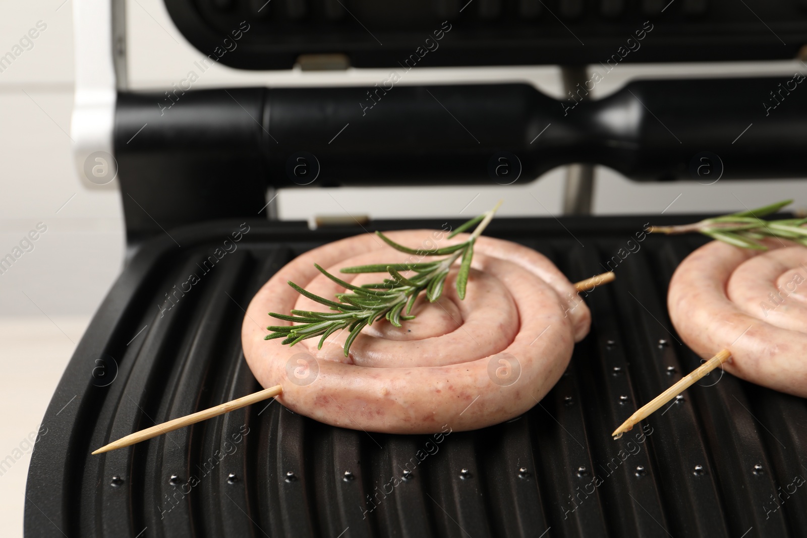 Photo of Electric grill with homemade sausages and rosemary on light background, closeup