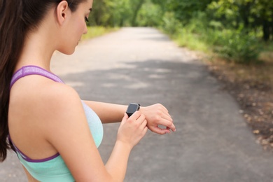 Young woman checking pulse with smartwatch after training in park. Space for text