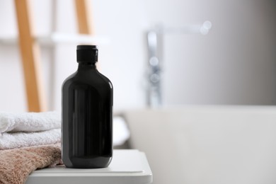 Photo of Bottle of bubble bath and towels on white table in bathroom, space for text