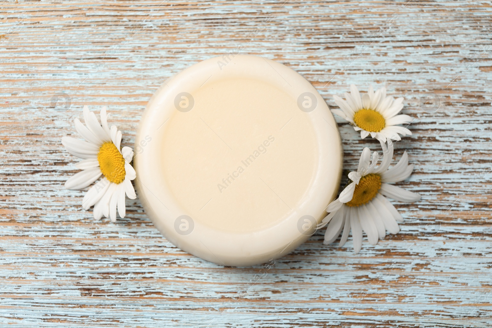 Photo of Solid shampoo bar and chamomiles on light wooden table, flat lay. Hair care