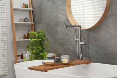 Photo of Shelving unit and wooden tub tray with different spa products in bathroom