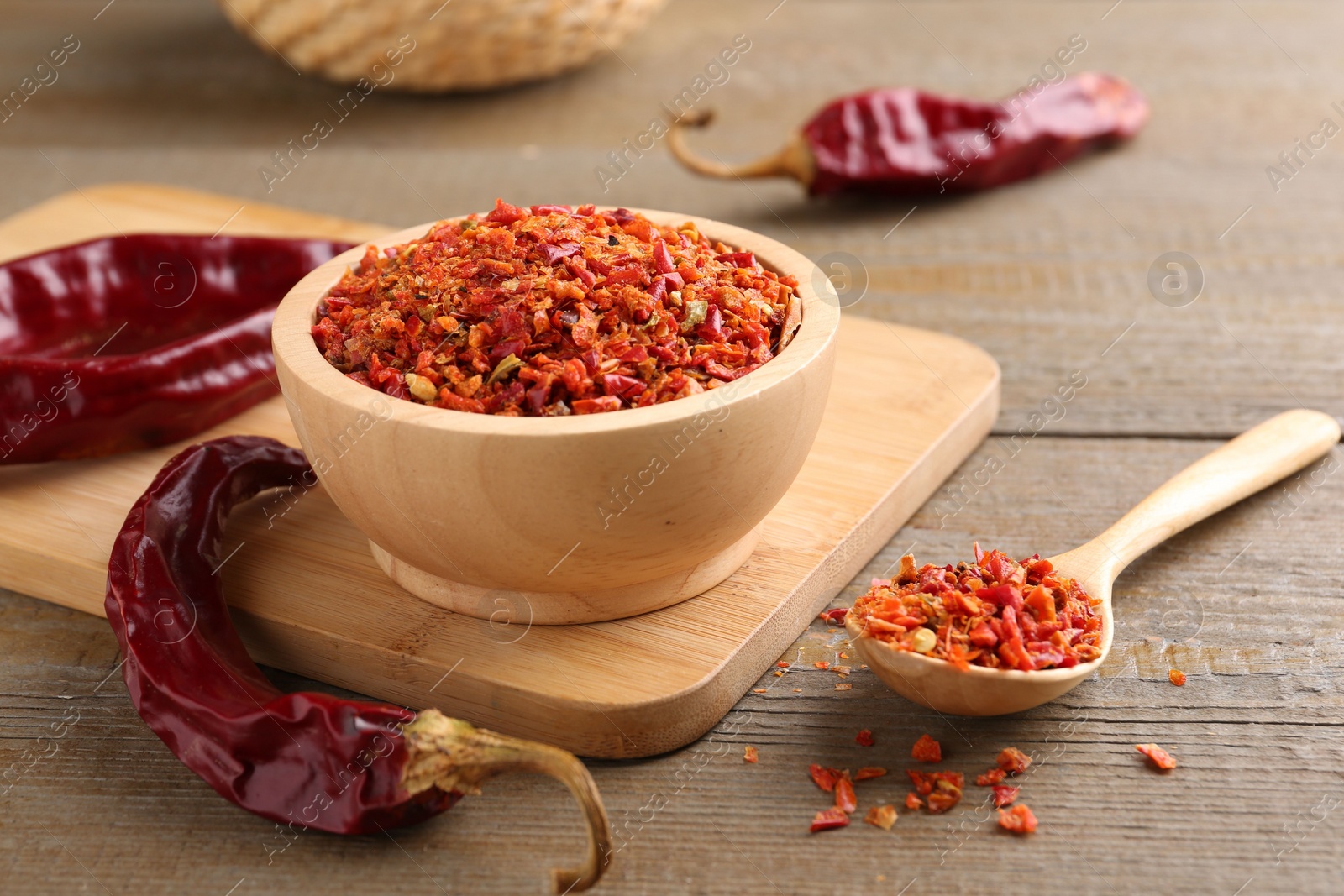 Photo of Aromatic spice. Red chili pepper flakes in bowl, spoon and pods on wooden table