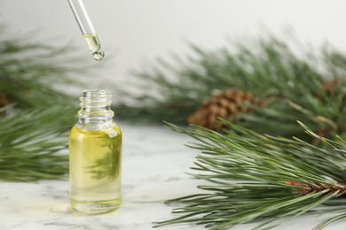 Dripping pine essential oil into bottle at white marble table. Space for text